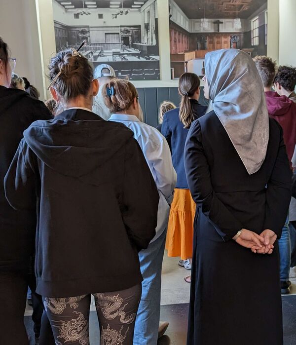 Eine Gruppe blickt auf ein aktuelles und ein historisches Foto des Saal 600. Bildnachweis: Geschichte Für Alle e.V.